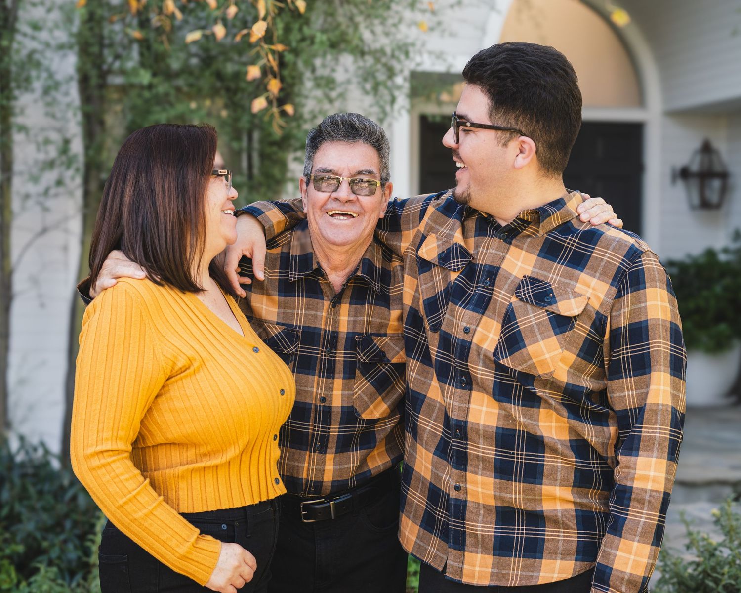 A couple in coordinating yellow sweater and plaid shirt embrace and laugh together outdoors during a photo session.