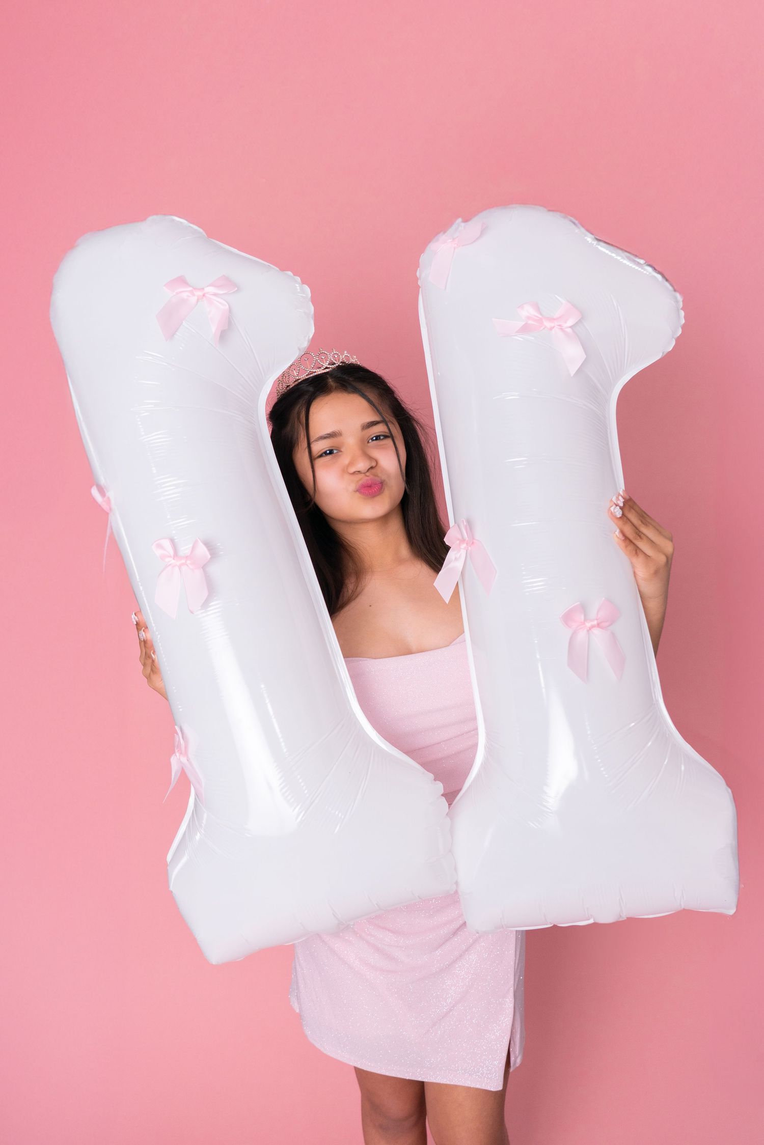 Child in pink dress holds large white decorative letters against pink background.