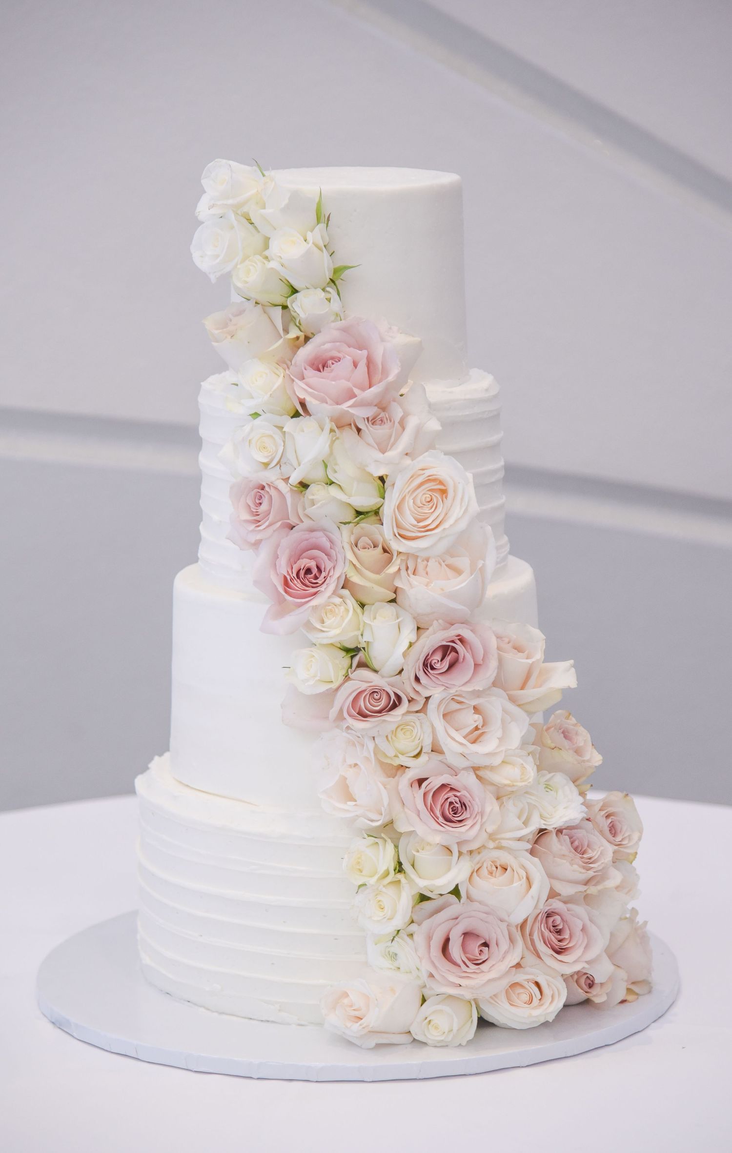 White wedding cake decorated with cascading pink and blush roses and delicate floral accents.