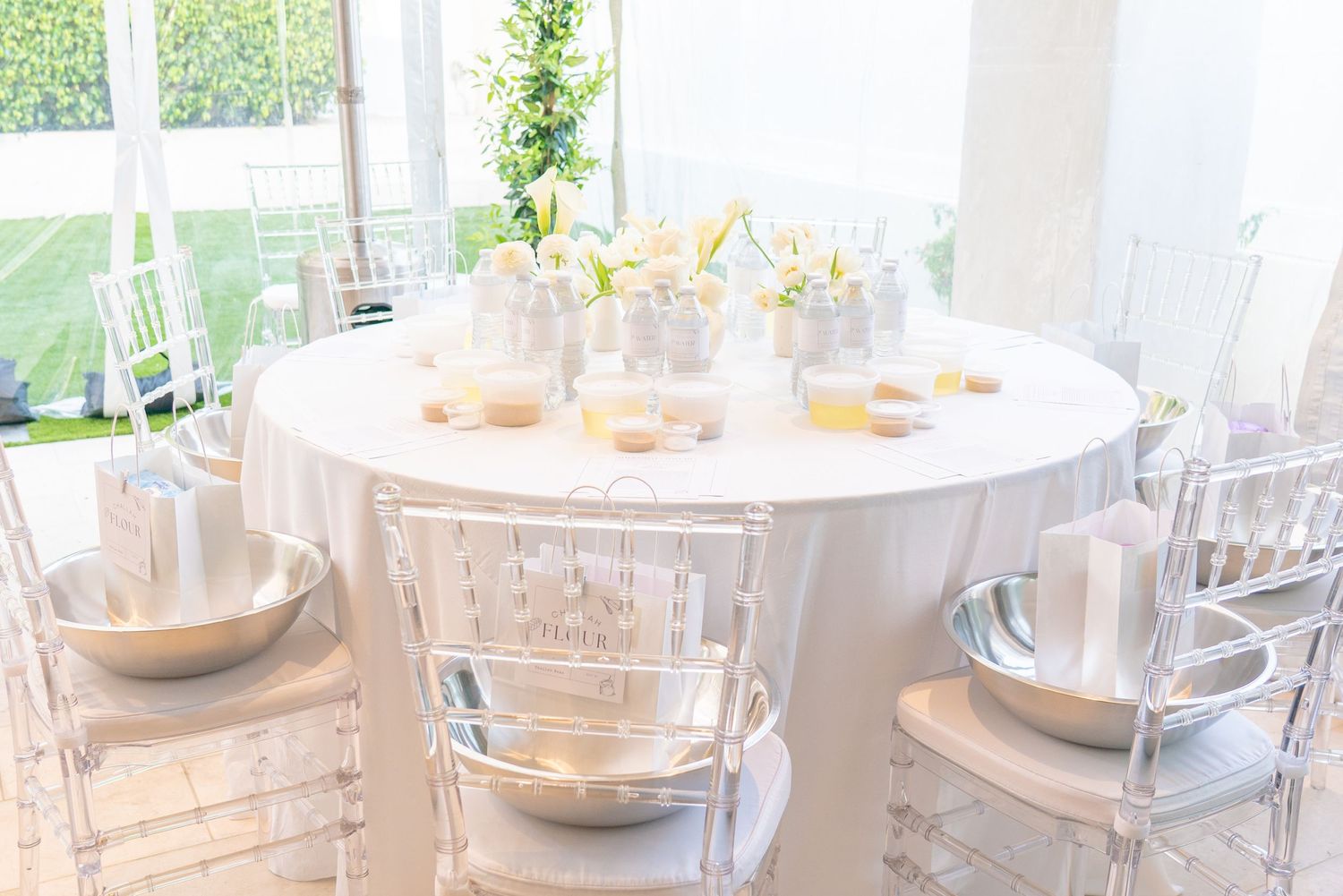 Elegant wedding reception table setting with white linens, clear ghost chairs, and soft natural lighting in a tent.