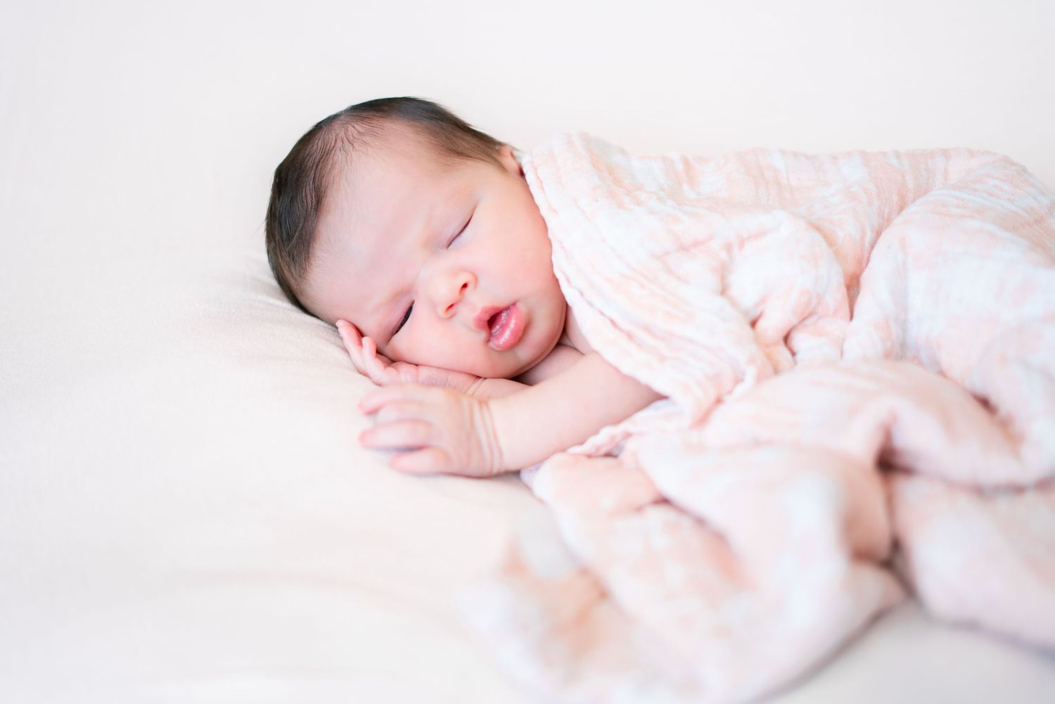 A sleeping newborn baby wrapped in soft pink fabric against a white background.