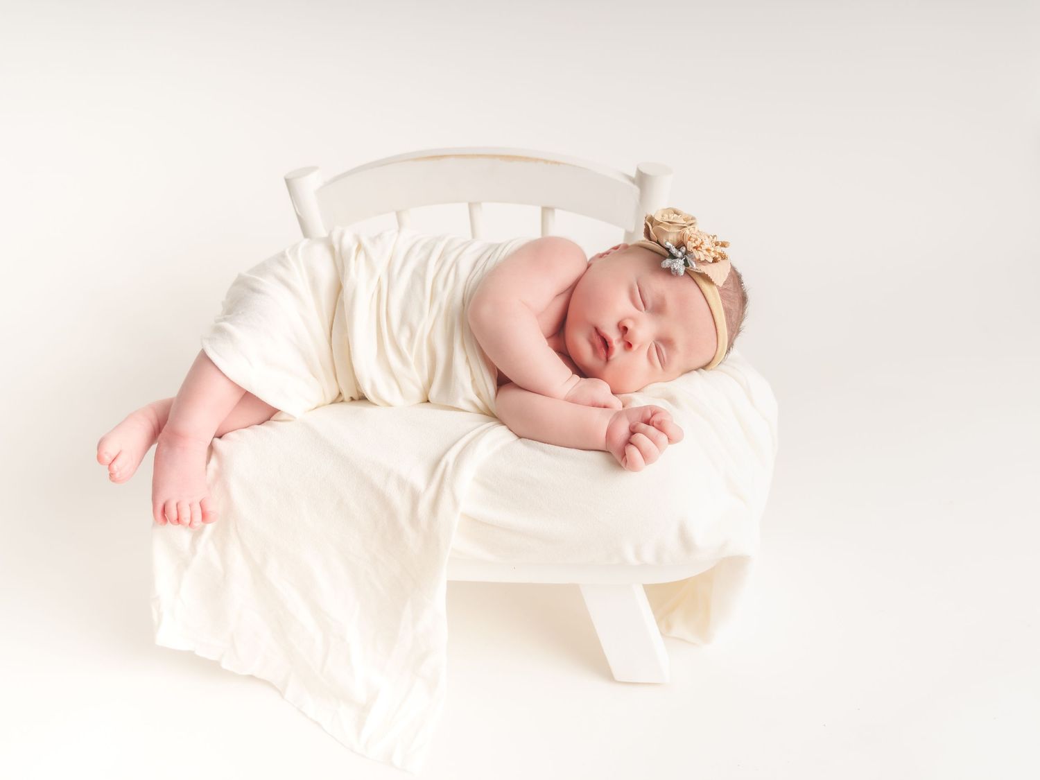Peaceful newborn sleeping in cream-colored wrap on white background.