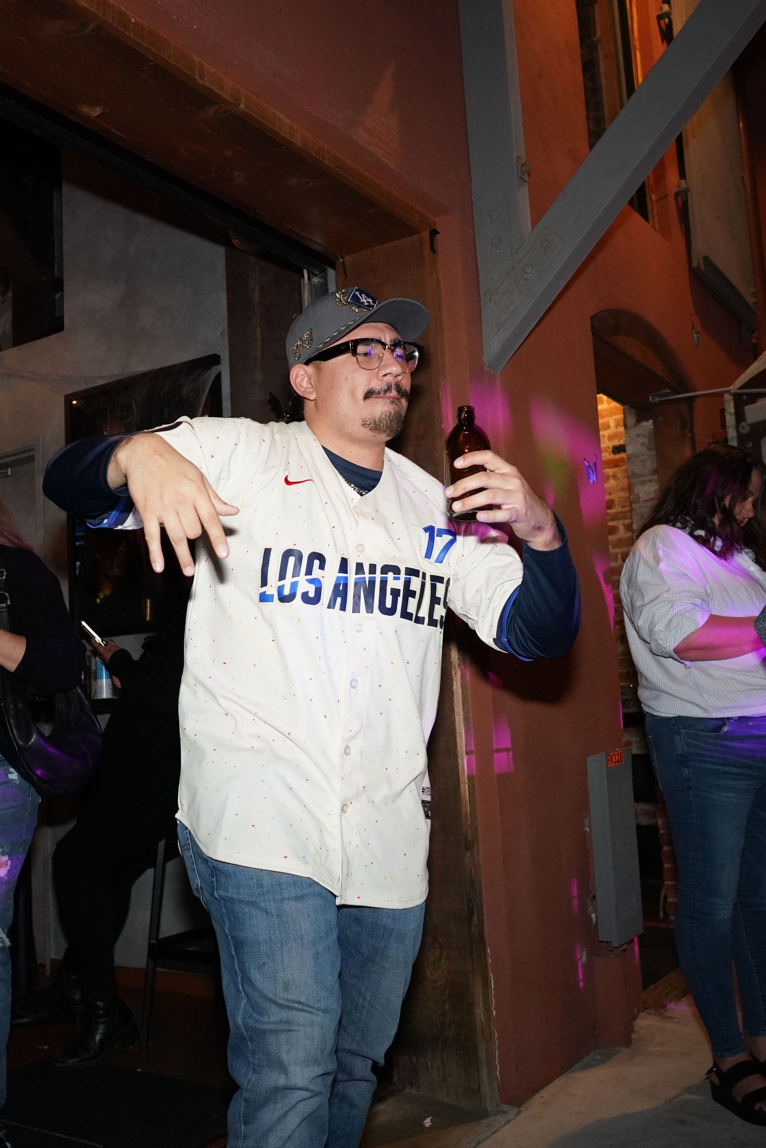 Man in Los Angeles Dodgers jersey holding a beer bottle at an outdoor nightlife event.