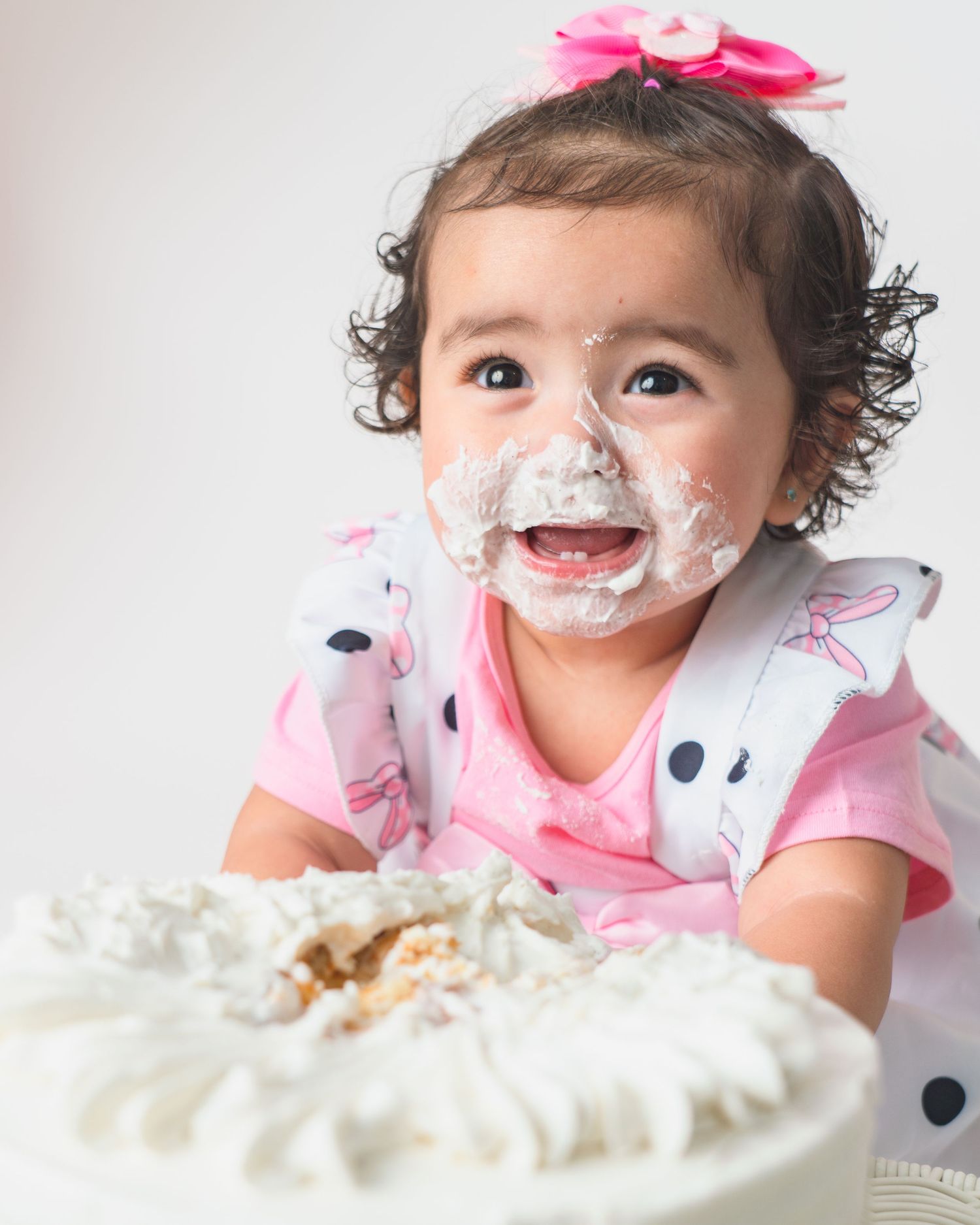 Baby with cake frosting on face smiles during first birthday cake smash photo session.