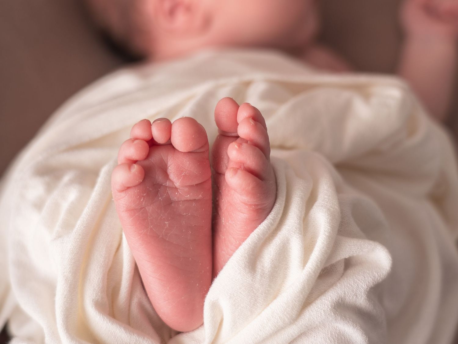 Close-up shot of tiny baby feet and toes against soft white fabric sheets.