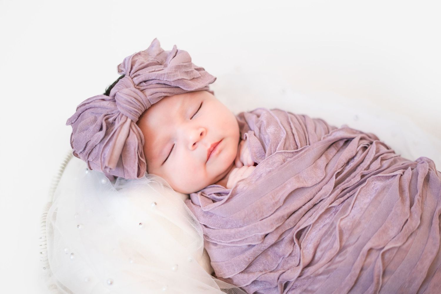 A newborn baby resting peacefully on white fabric with purple draping.