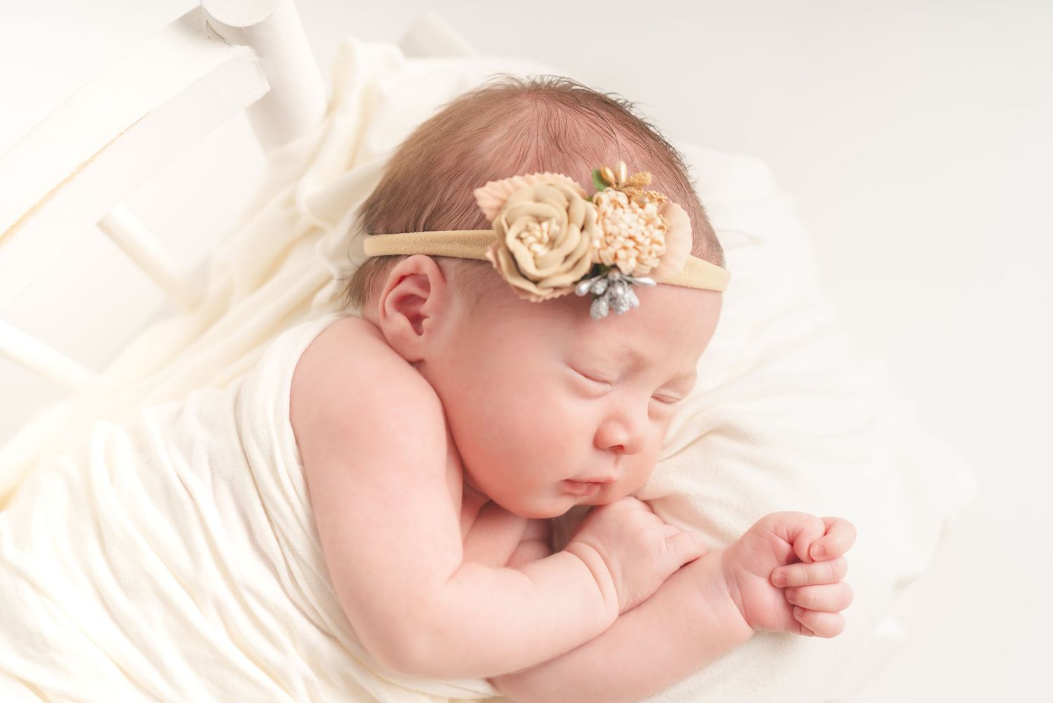 Newborn sleeping on cream fabric with delicate floral headpiece.