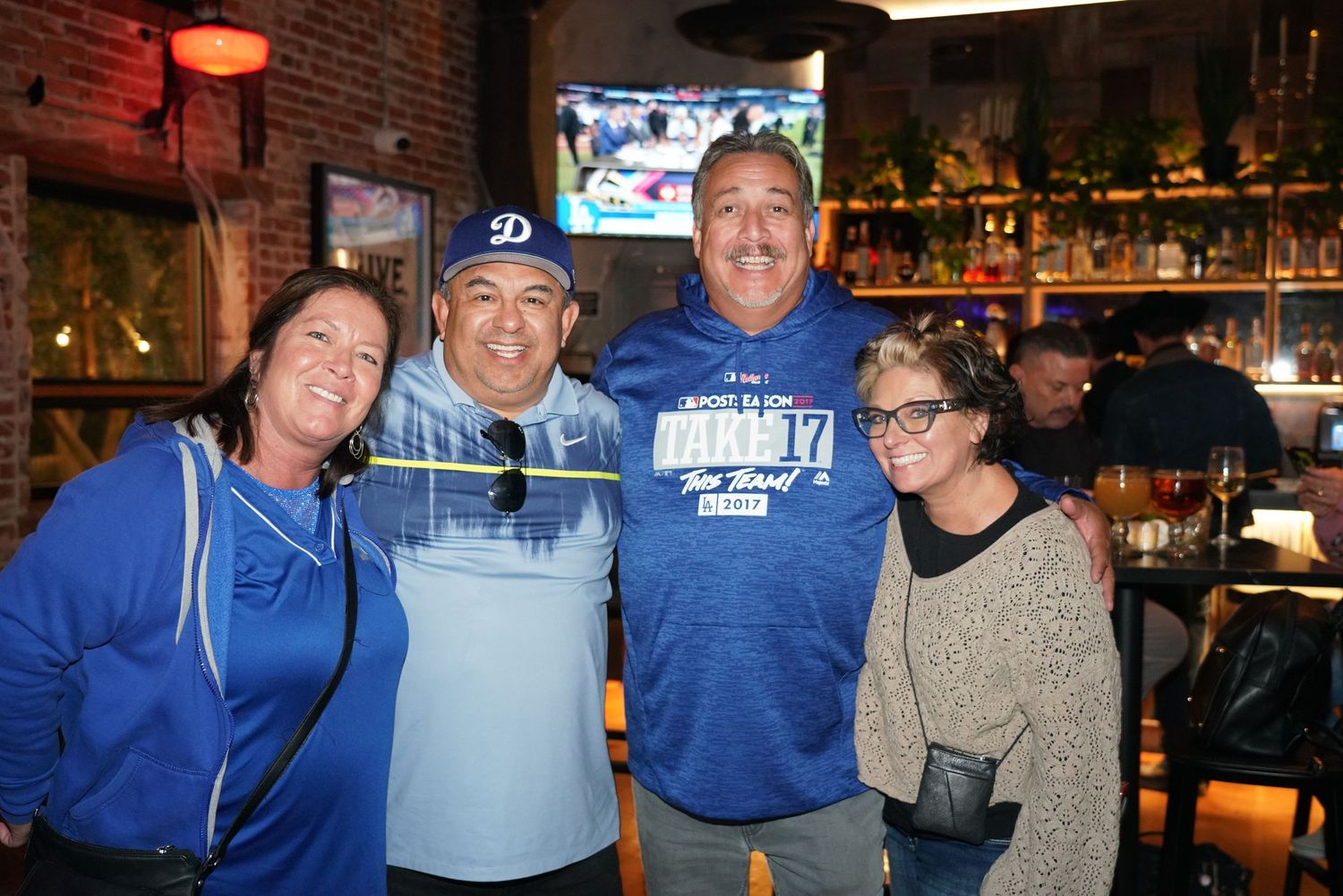 Four friends pose together at a sports bar wearing Los Angeles Dodgers blue gear during a game night.