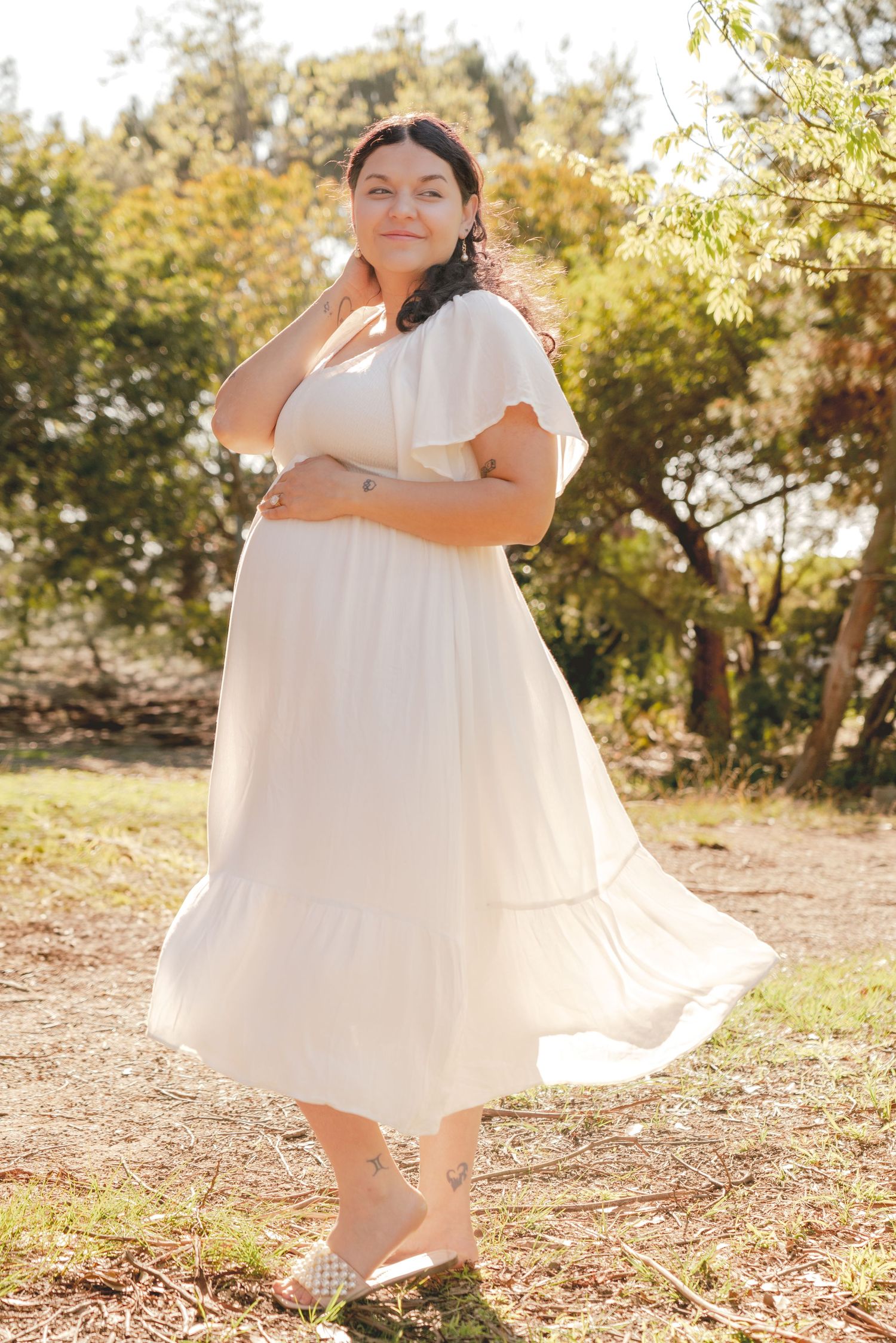 A flowing white dress twirls gracefully in a sun-dappled outdoor setting during a joyful spinning motion.