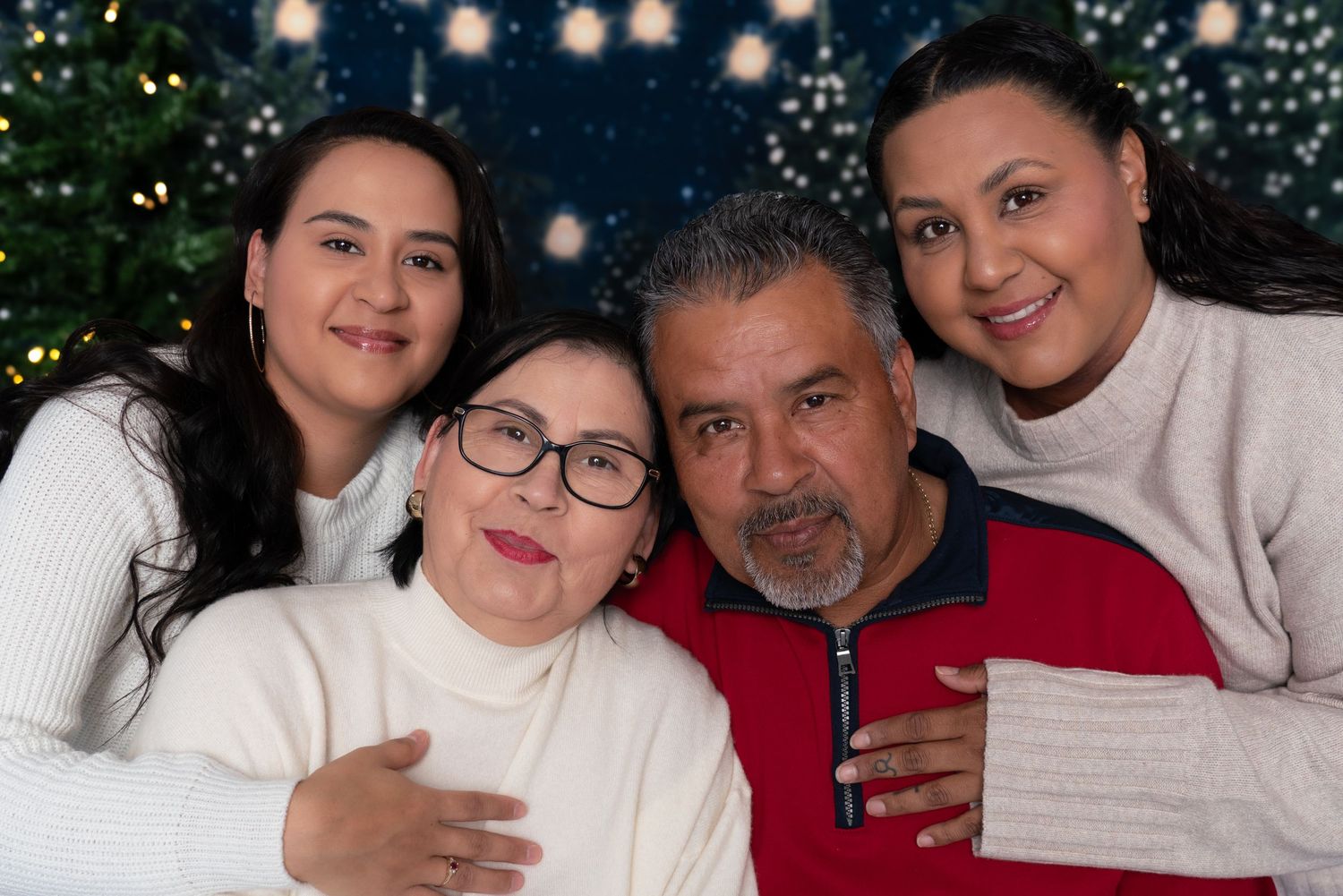 A family poses together for a holiday portrait with a Christmas tree and twinkle lights in the background.