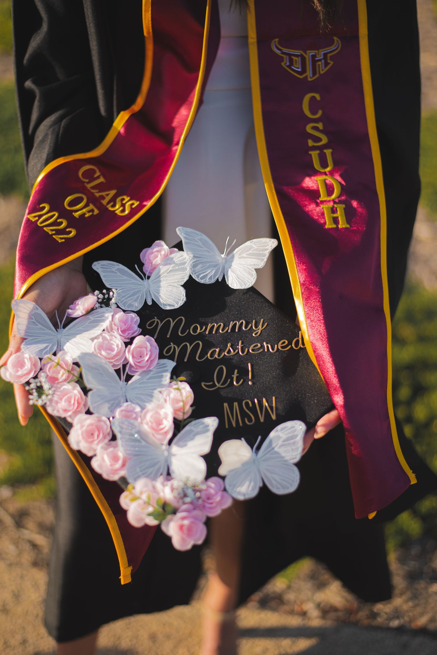 Graduation cap decorated with pink and white flowers and text written in gold.
