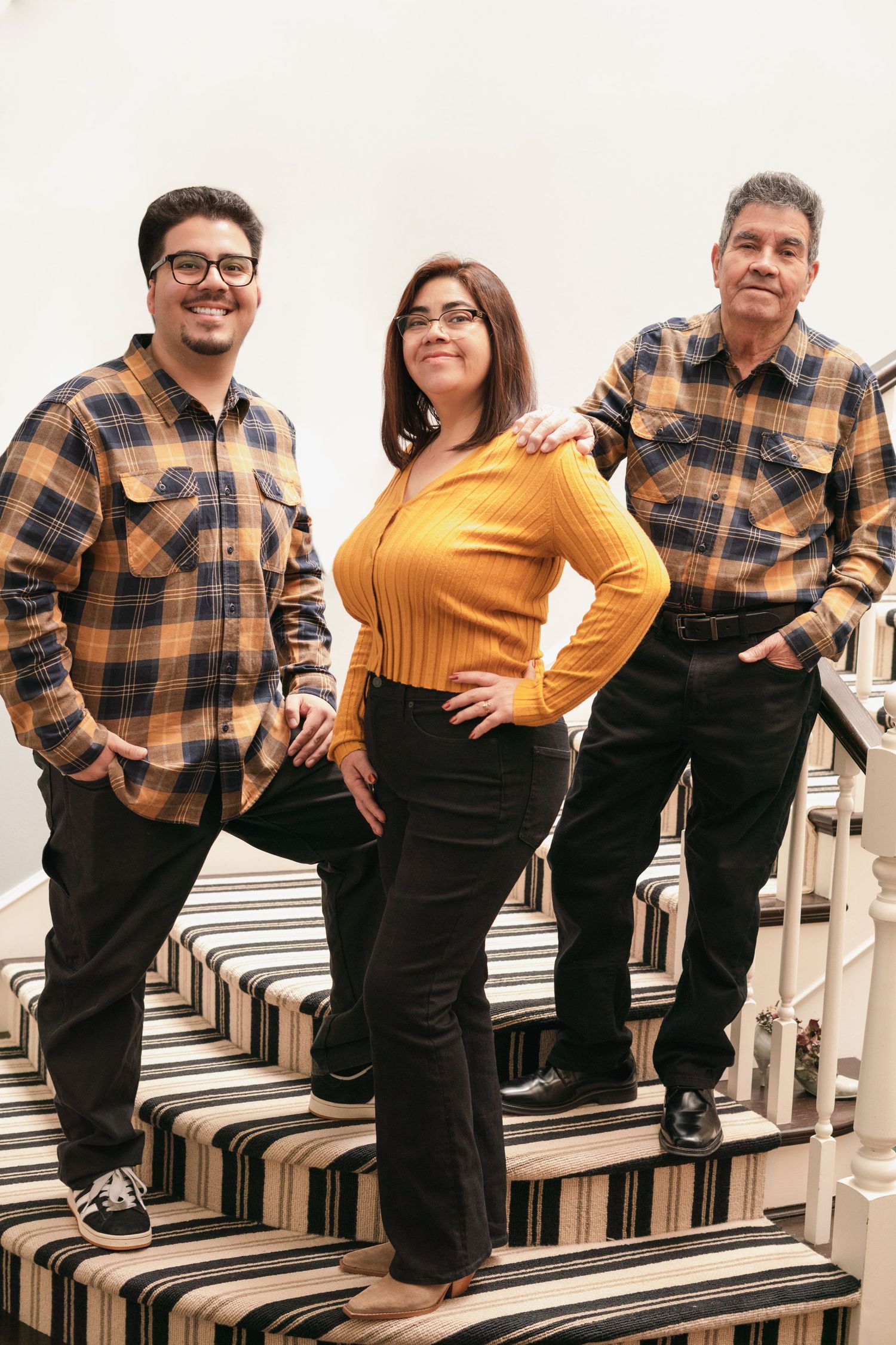 Family posing on striped carpeted stairs wearing coordinated plaid shirts and yellow sweater.