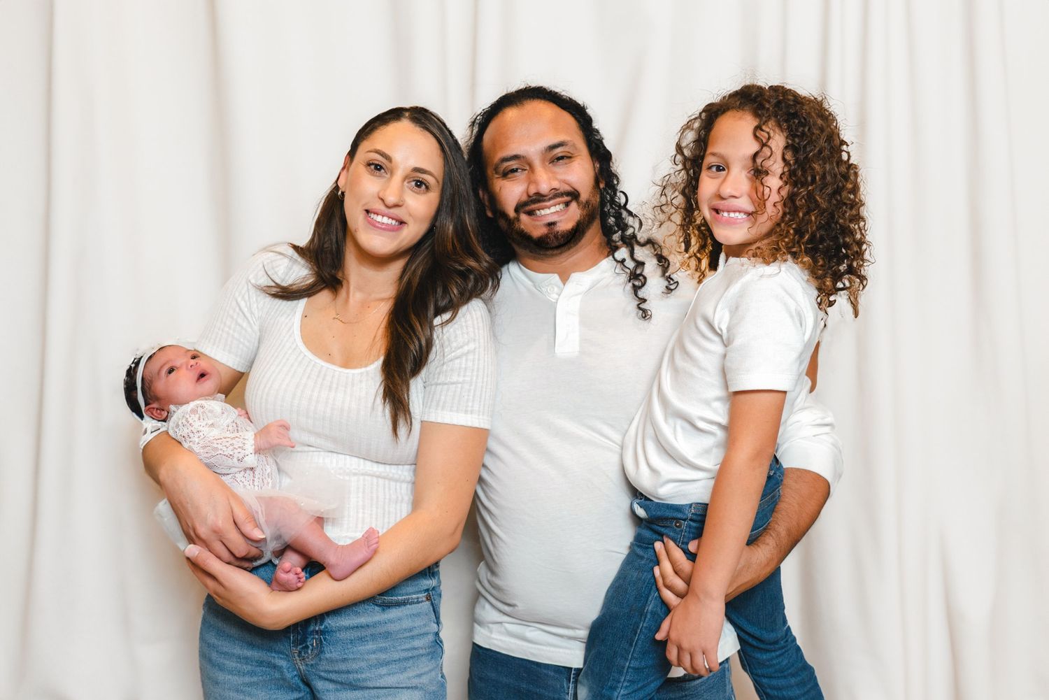 Family portrait session with coordinated white shirts and blue jeans against white backdrop.