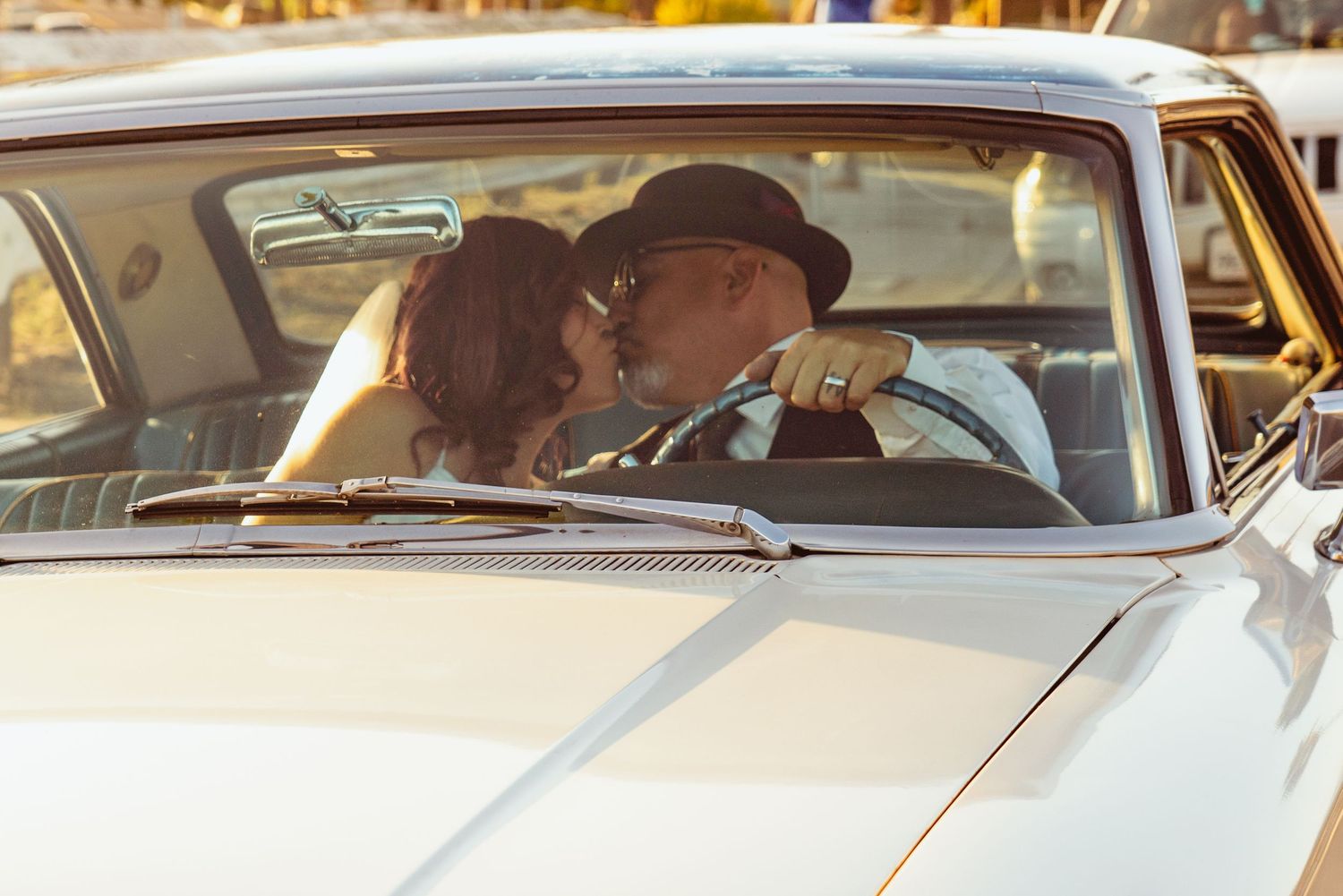 Couple sharing a romantic kiss inside a vintage white classic car, evoking a timeless retro love story.