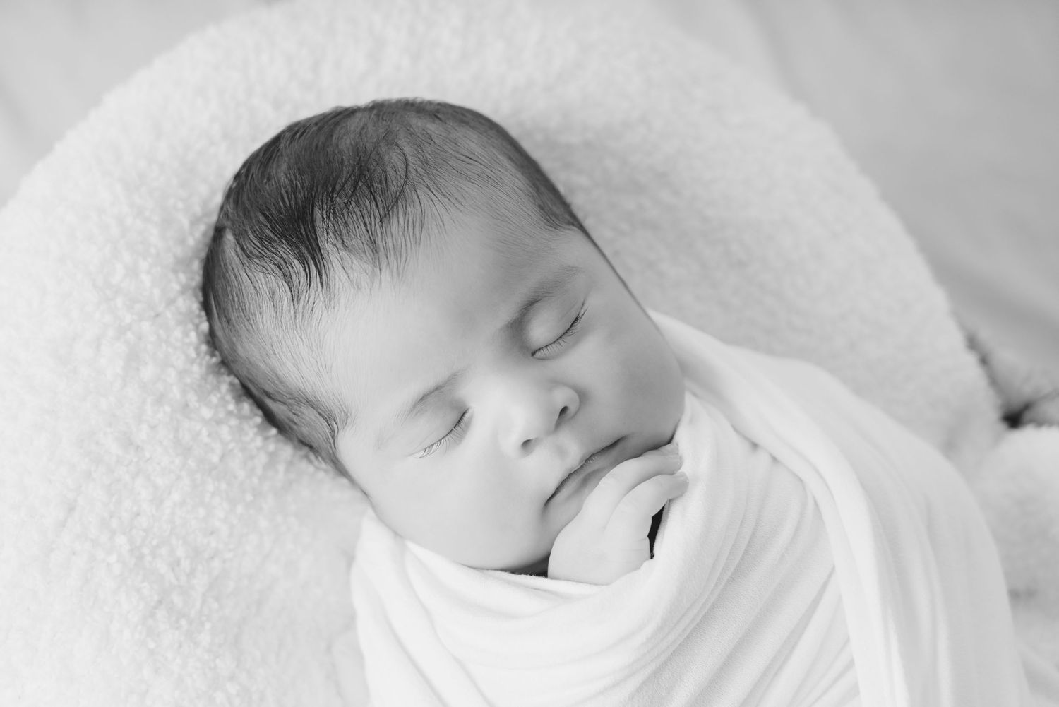Black and white photo of a peaceful sleeping newborn baby wrapped in a white swaddle blanket.