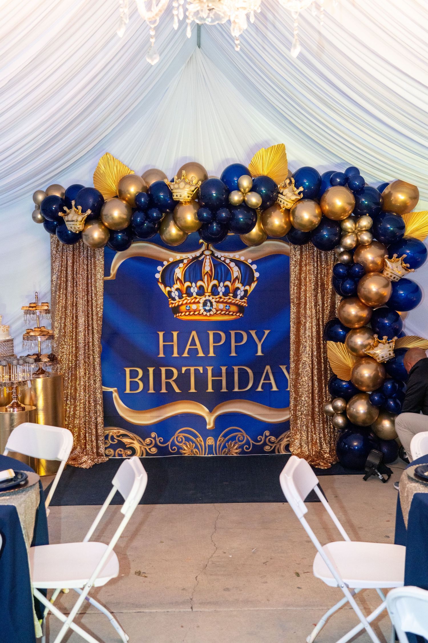 Royal blue and gold birthday party setup with balloon garland and crown decorations.