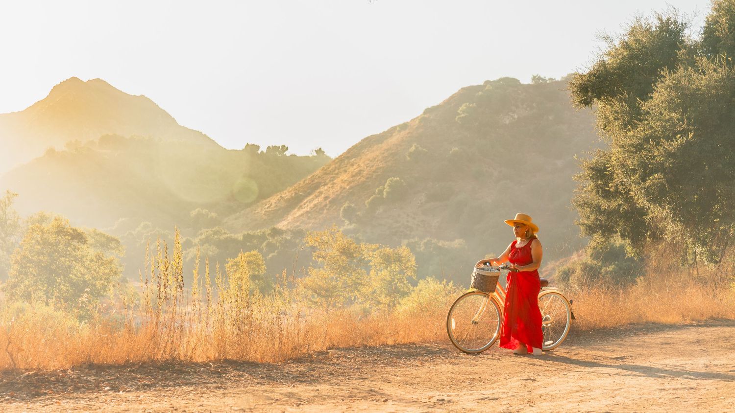 A person in red clothing sits meditatively on a mountain trail during golden hour with scenic mountain views.