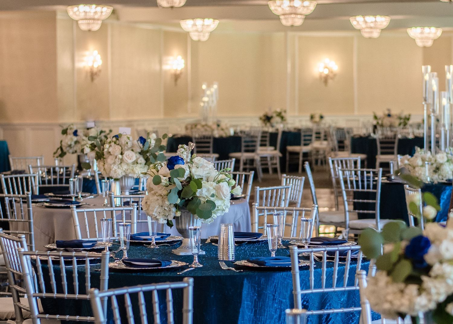 An elegant reception hall with crystal chandeliers and navy blue and white table settings.