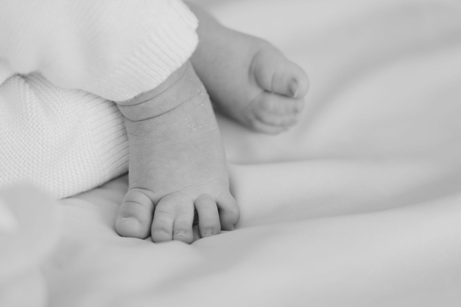 Close-up black and white photo of tiny newborn baby feet resting on soft white blanket.