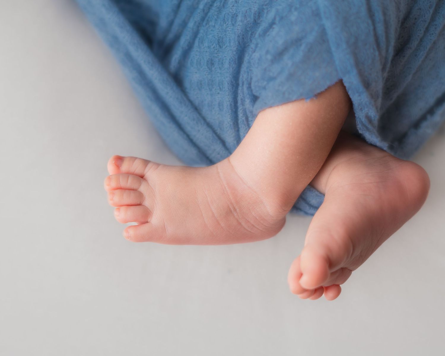 Close-up of tiny baby feet peeking out from a soft blue blanket on a white background.