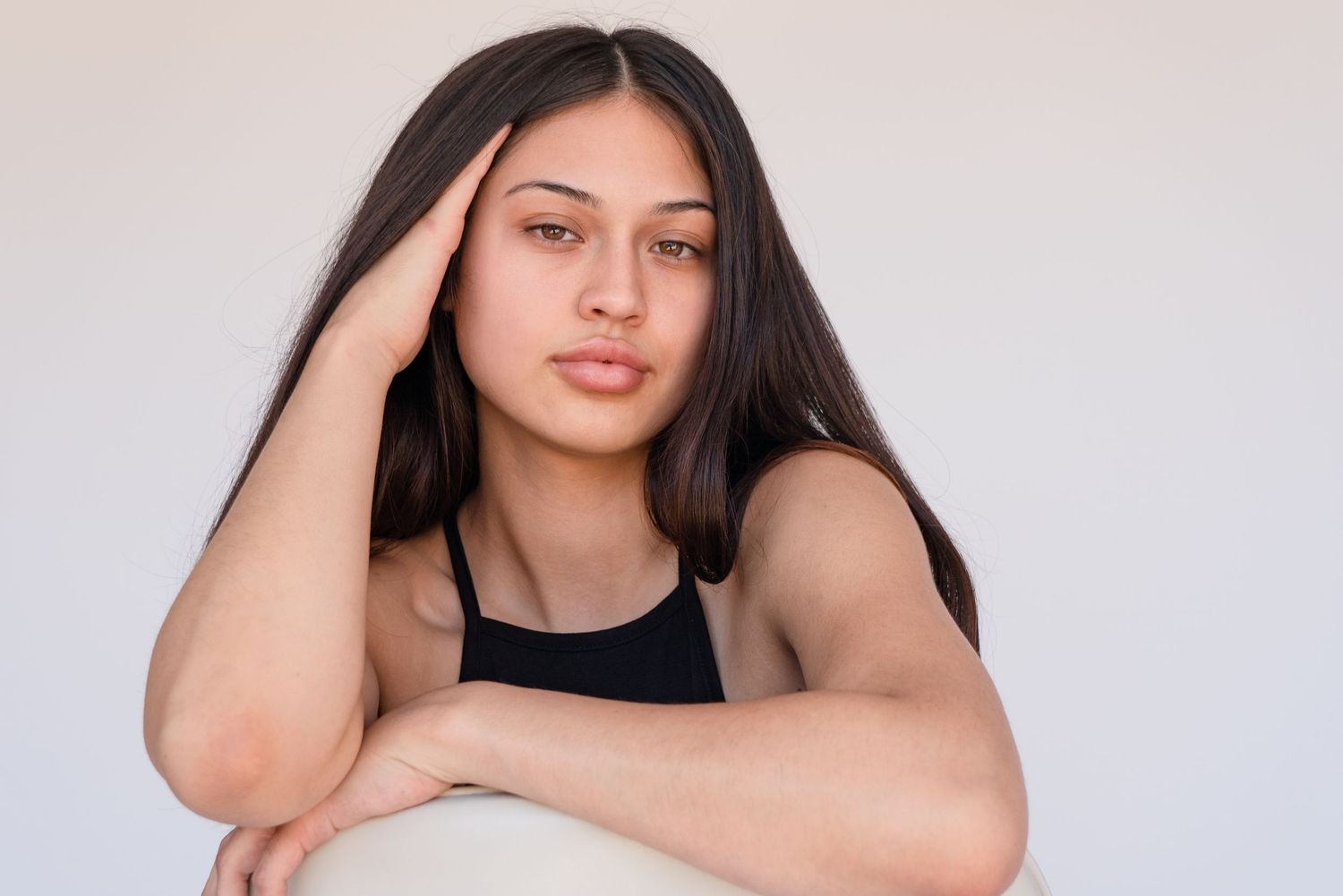 A person with long dark hair poses in a black top against a light background in a professional photo series.