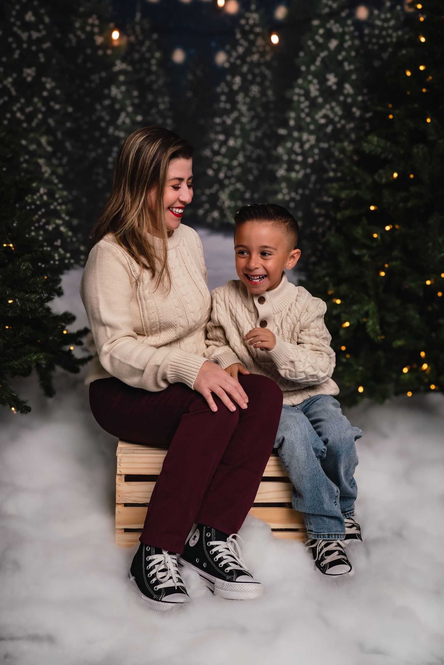 Two people share a joyful moment sitting on a bench surrounded by fog and twinkling Christmas lights in the background.