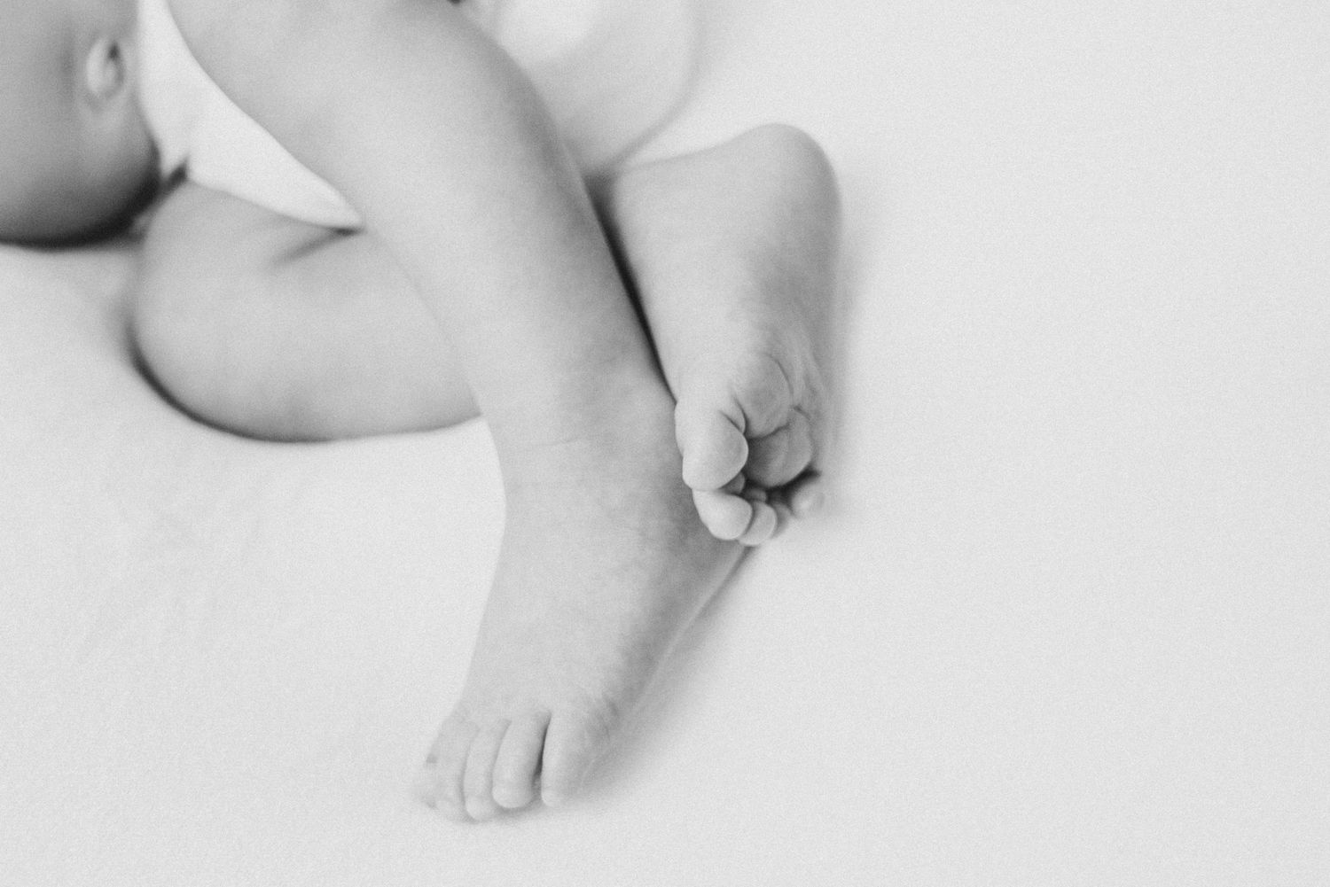 Black and white artistic detail shot of tiny baby feet and legs.