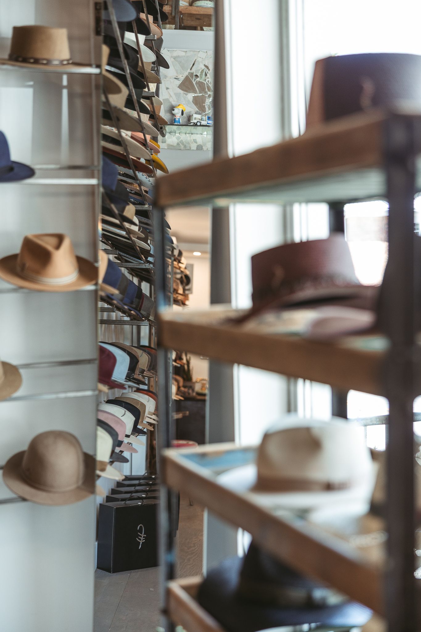 Des rangées de chapeaux fedora bruns et élégants sont exposées sur des étagères en bois, à l’intérieur d’une chapellerie baignée de lumière