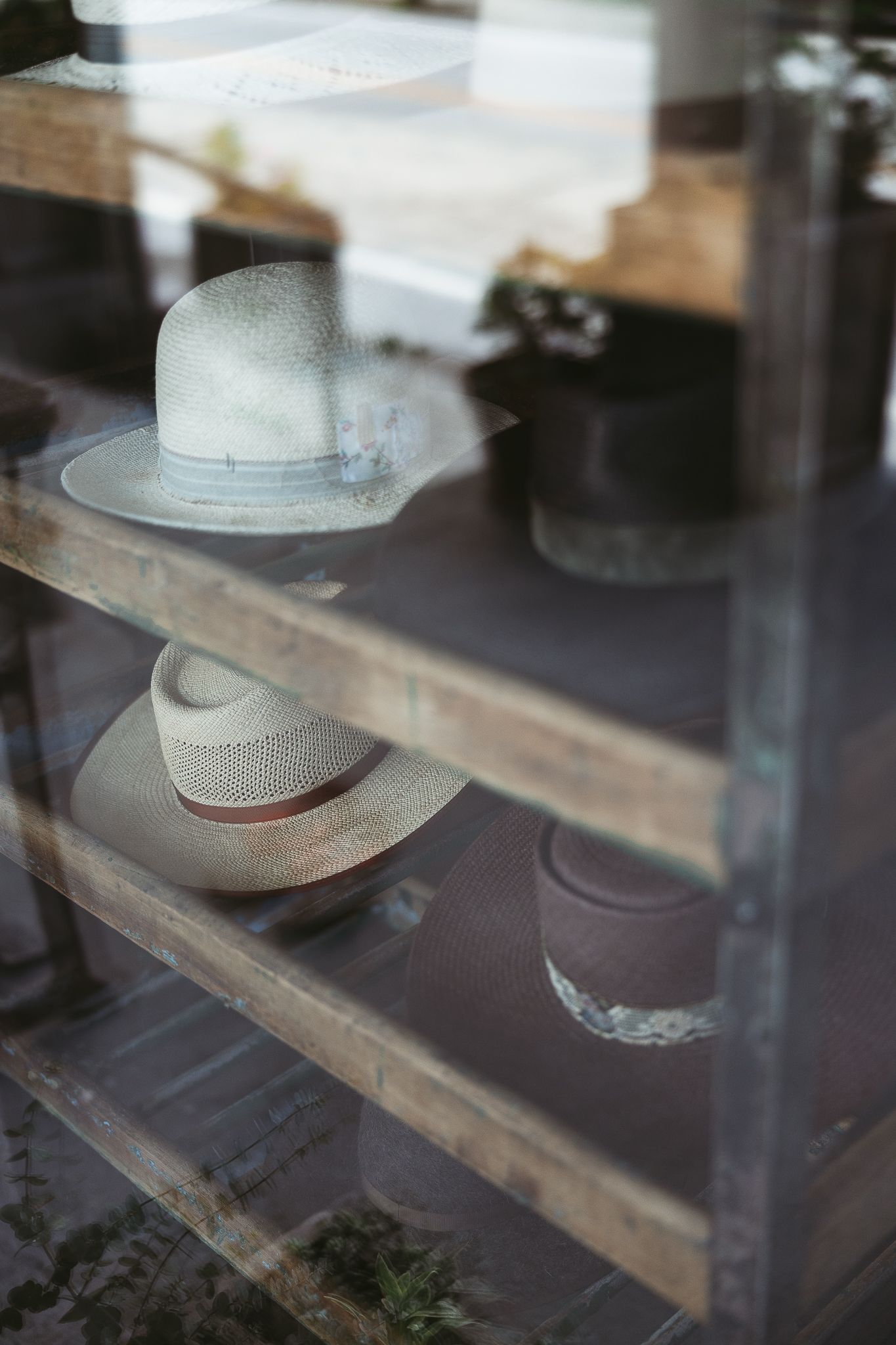 Une collection de chapeaux de paille aux teintes claires est exposée sur des étagères en bois derrière des vitrines en verre.