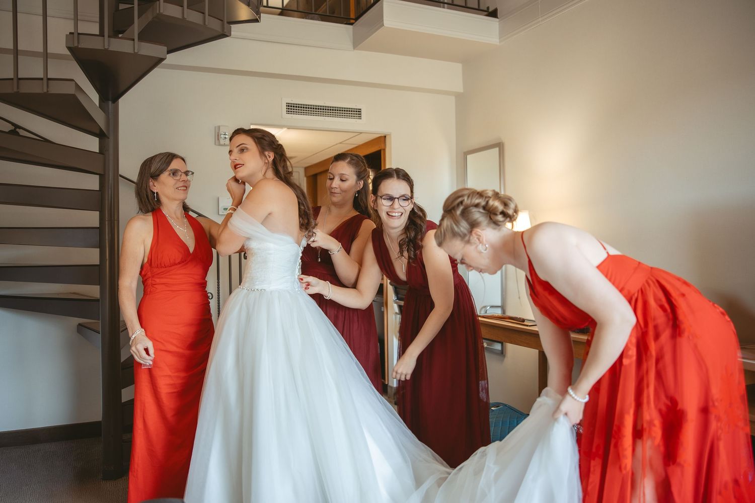 Bridesmaids in vibrant red dresses help the bride prepare in an elegant getting ready room.