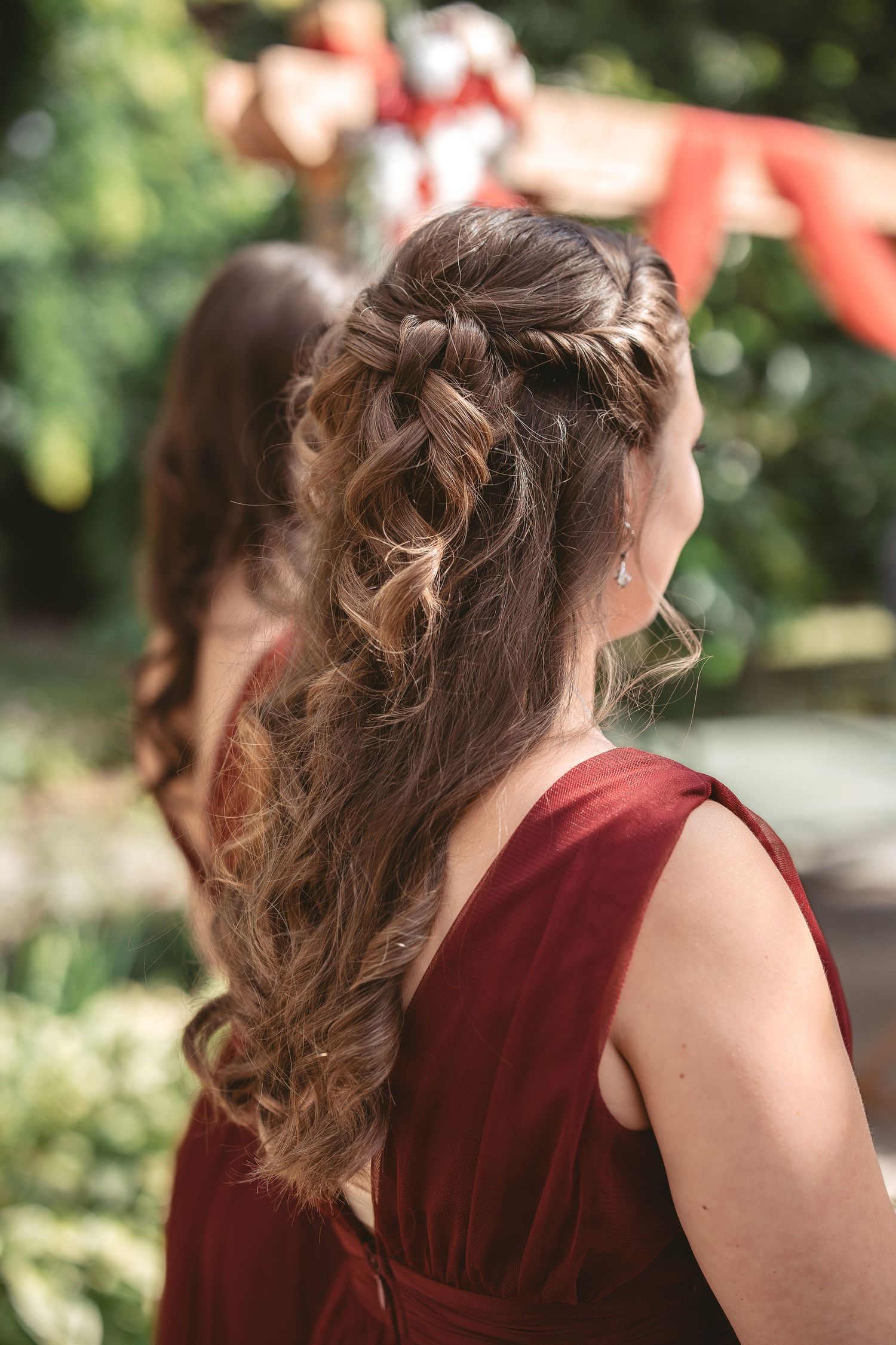 Elegant hairstyling detail showing intricate braids and curls in burgundy-toned outdoor setting.