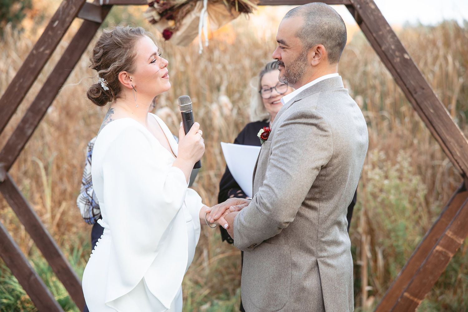 Échange de voeux lors d'un mariage en plein air au cœur d’une forêt automnale, baignée d’une lumière dorée filtrant à travers les arbres.