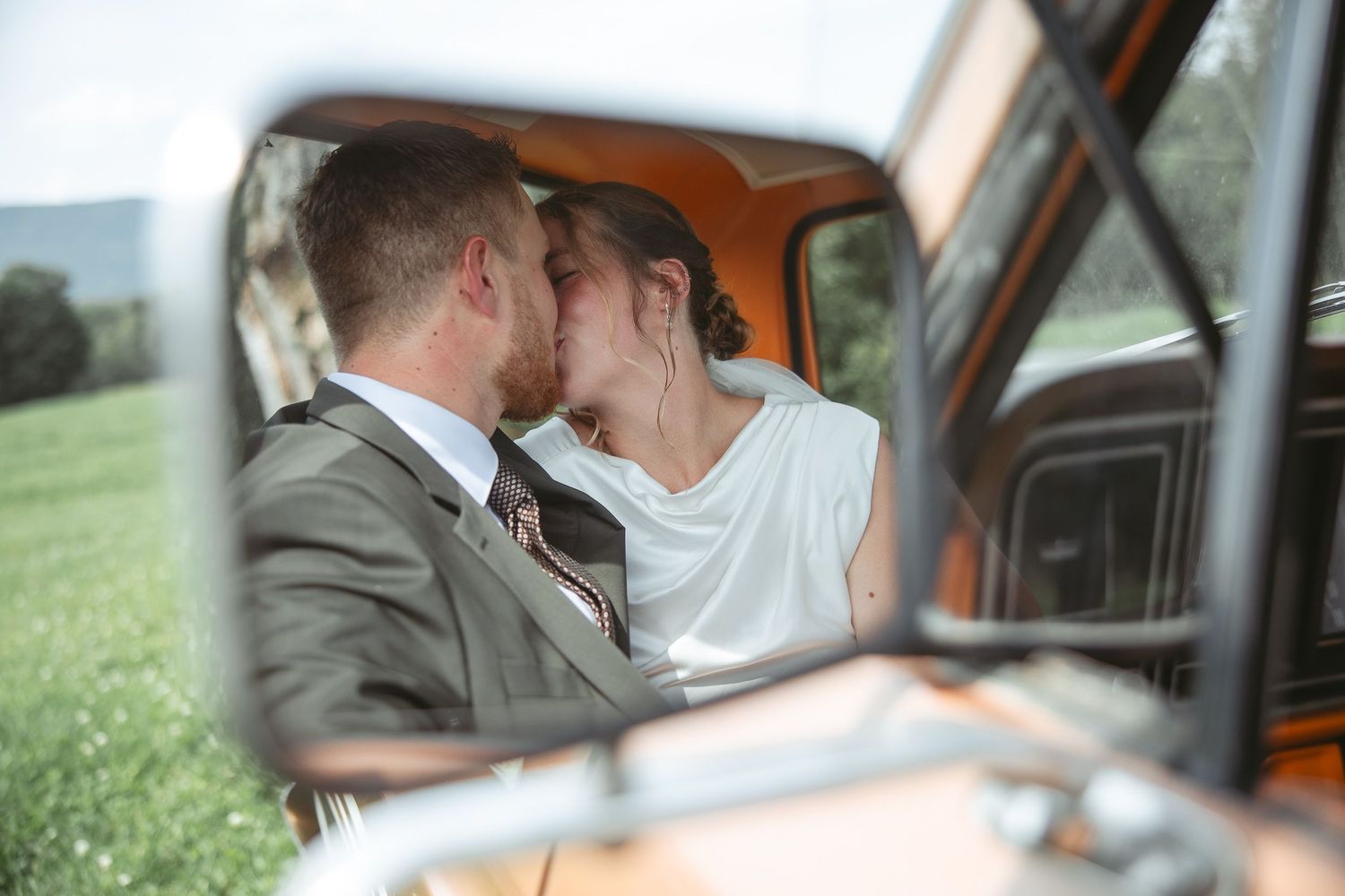 Moment romantique capté à travers la vitre d’une voiture vintage, avec un champ verdoyant en arrière-plan