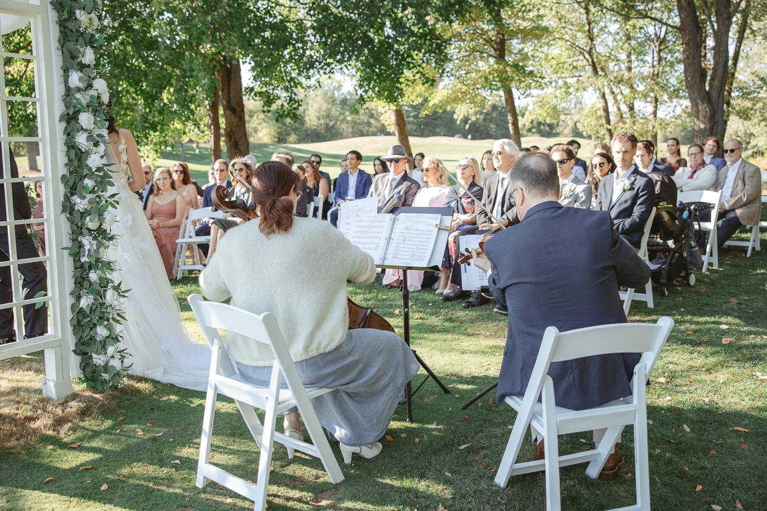 Invités de mariage assis à des tables en extérieur sous les arbres lors d’une réception de jardin en journée