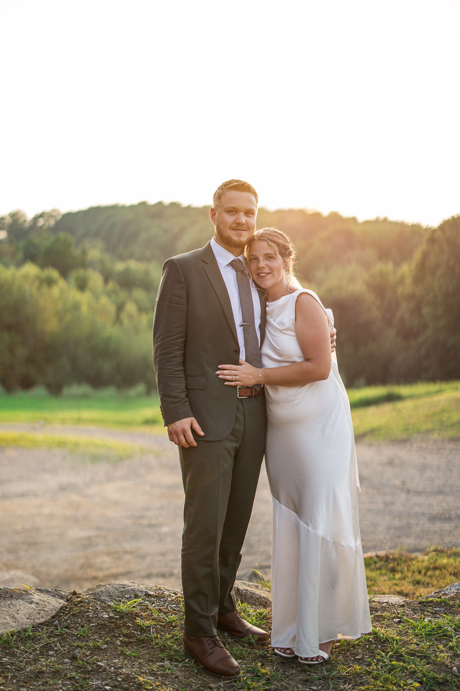 Couple romantique posant ensemble au coucher du soleil dans un champ, vêtu de tenues de mariage élégantes