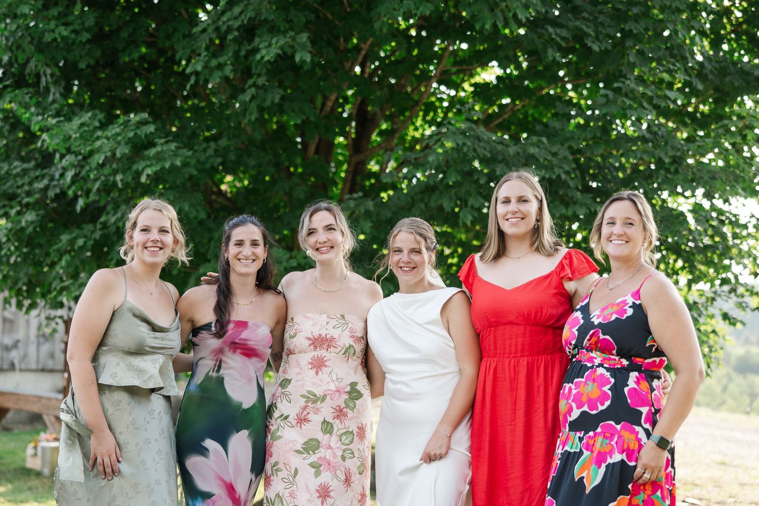 Groupe en robes fleuries colorées et tenues d’été posant ensemble en extérieur sous des arbres verdoyants