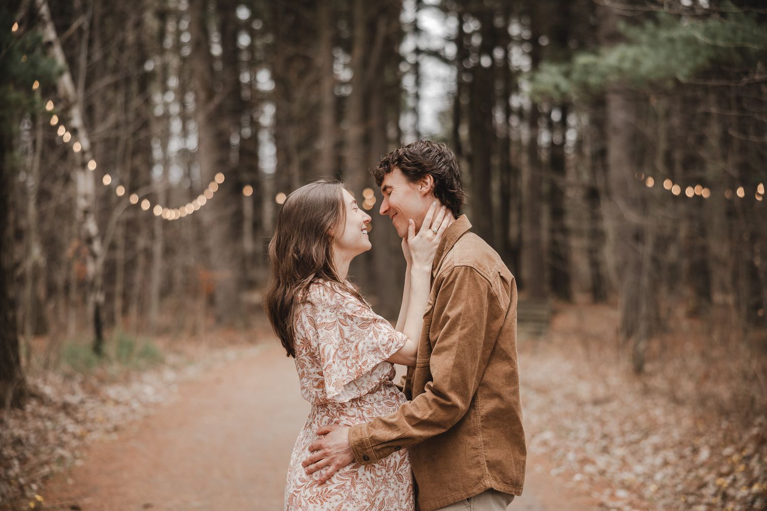 Couple romantique s’enlaçant sur un sentier boisé, guirlandes lumineuses dans une forêt d’automne, en Estrie