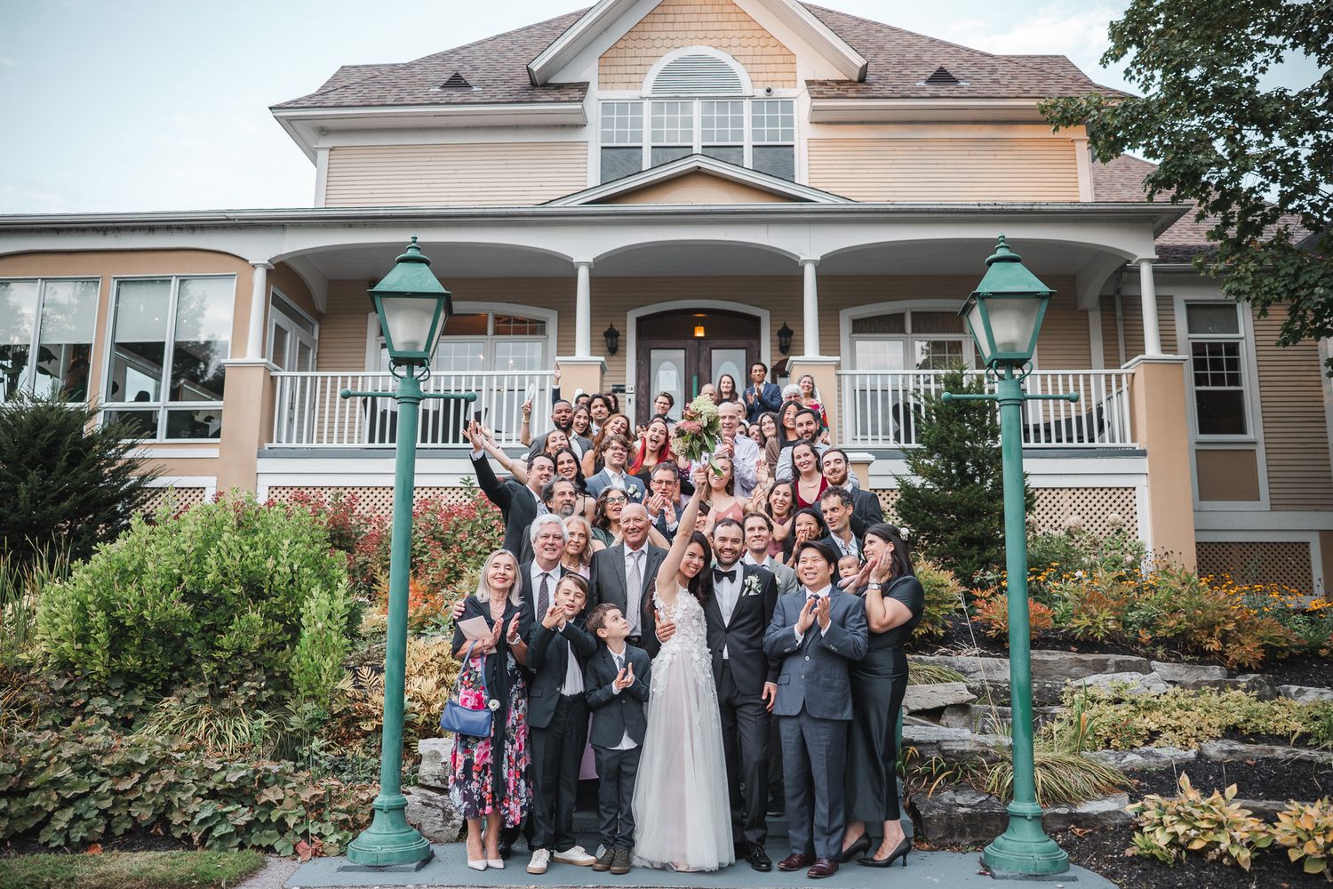 Grand cortège de mariage réuni sur les marches d’une élégante maison victorienne rose avec galerie et lampadaires verts
