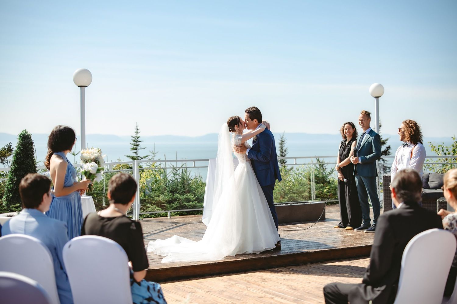 Couple de mariés qui s'embrassent lors de leur cérémonie de mariage en plein air, dans un décor naturel et panoramique.