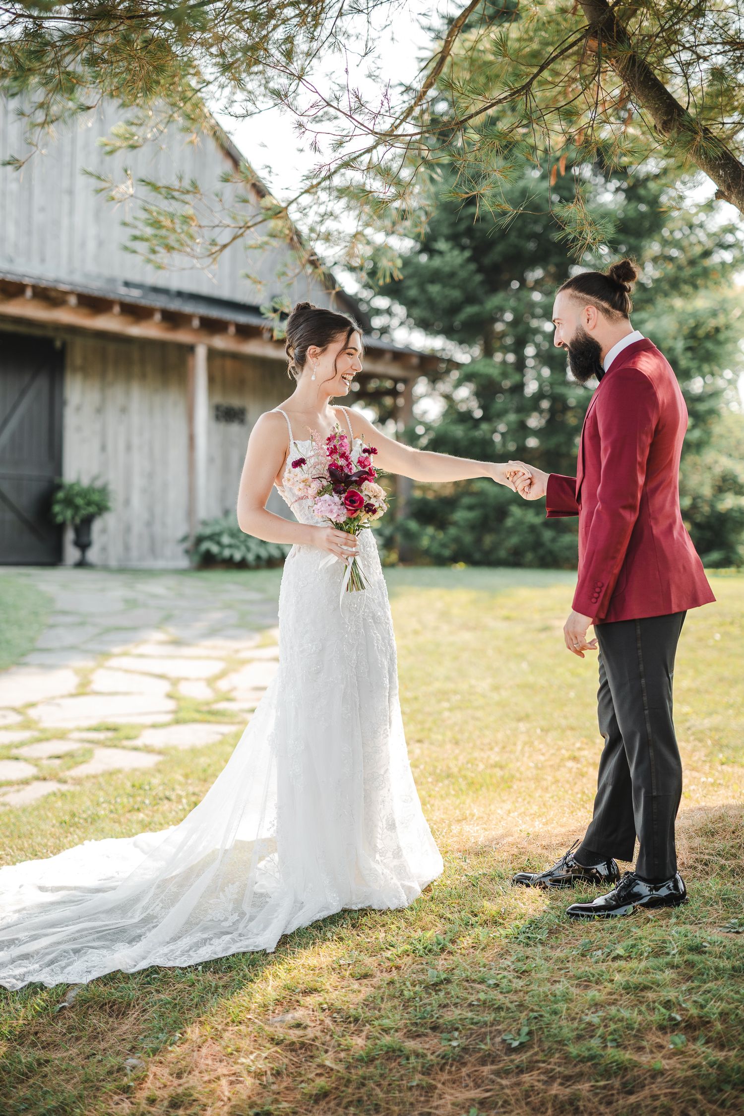 A romantic first look moment between a couple in formal wedding attire on a grassy hillside with a rustic barn in the background.