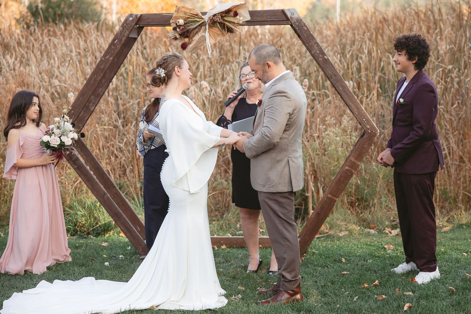 Échange de voeux lors d'un mariage en plein air au cœur d’une forêt automnale, baignée d’une lumière dorée filtrant à travers les arbres.