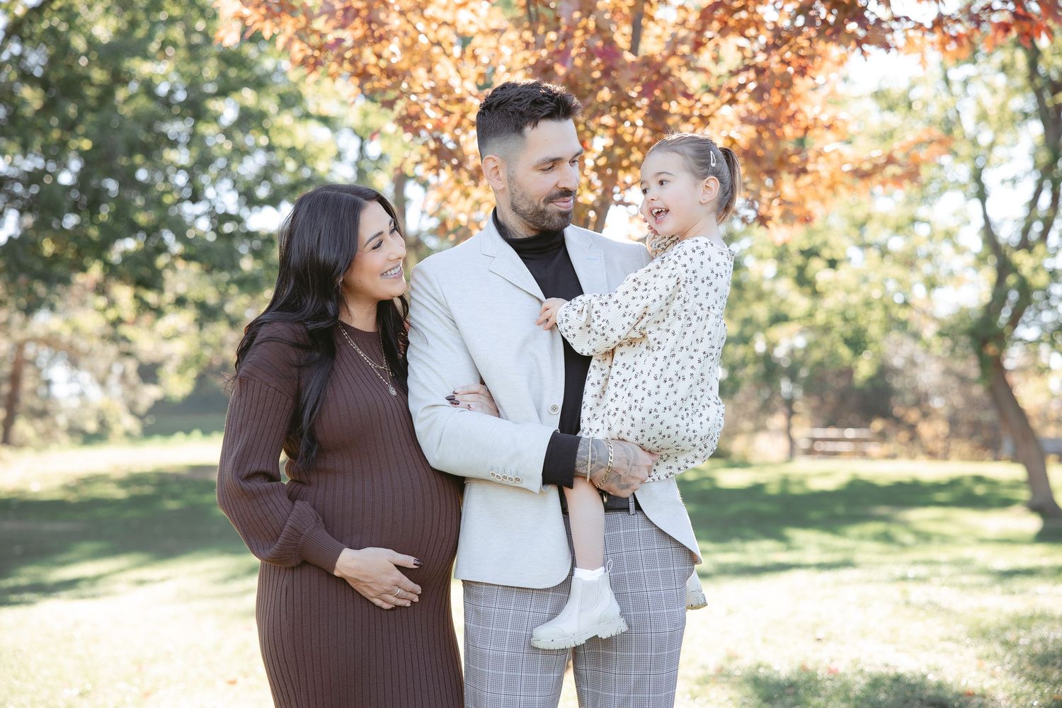 Family enjoying a warm autumn day together in a park with colorful fall foliage in the background.
