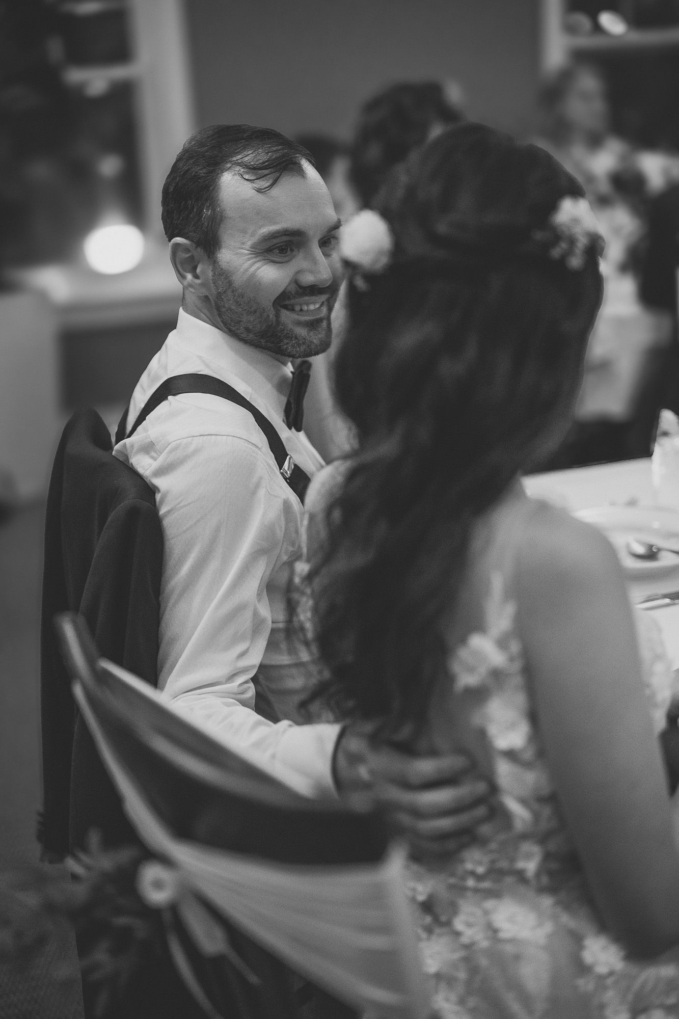 Moment spontané de réception de mariage en noir et blanc, interaction joyeuse entre deux personnes à table