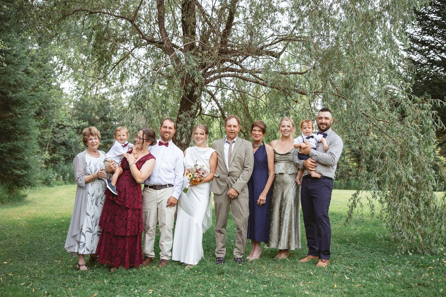 Cortège de mariage posant en extérieur sous des saules dans un jardin naturel