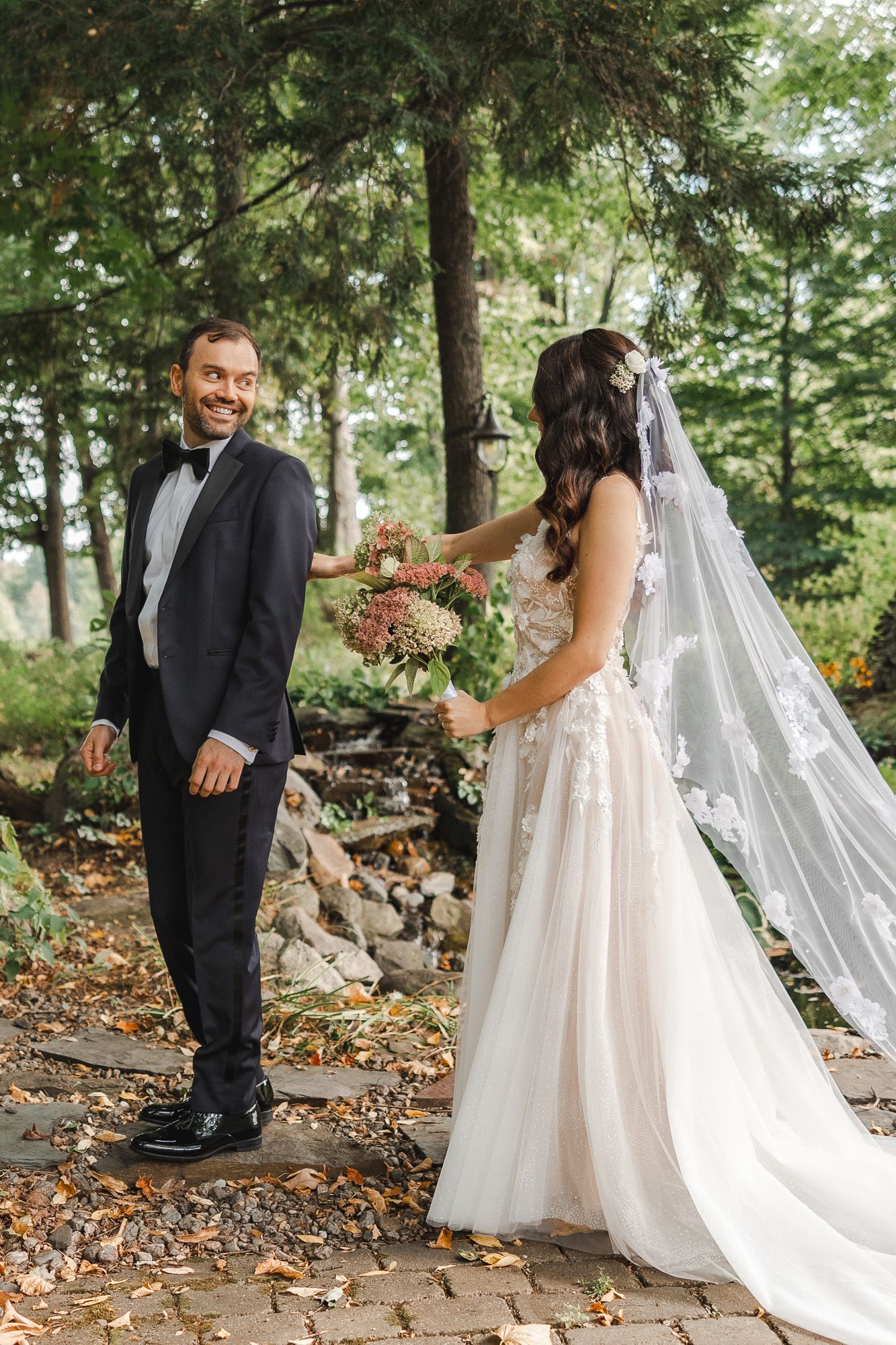 Mariée en robe blanche fluide et voile partageant un moment tendre avec son marié parmi les feuilles d’automne en forêt, en Estrie