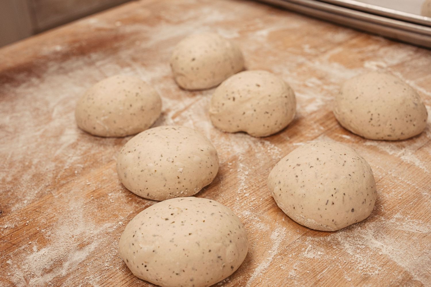Raw bread dough portions lined up on floured surface during preparation.