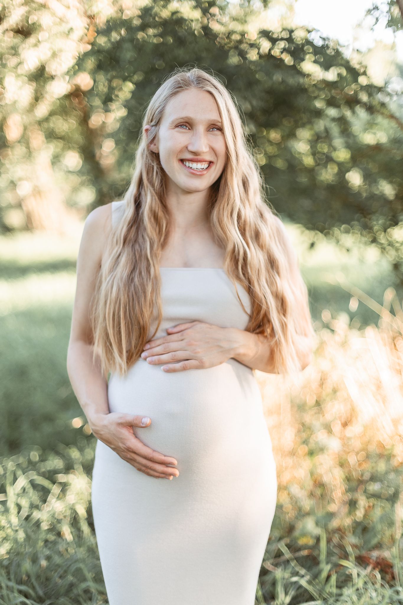 Séance maternité à Bromont/Estrie : femme enceinte en robe blanche à l’extérieur au coucher du soleil, capturée pour élégance et douceur