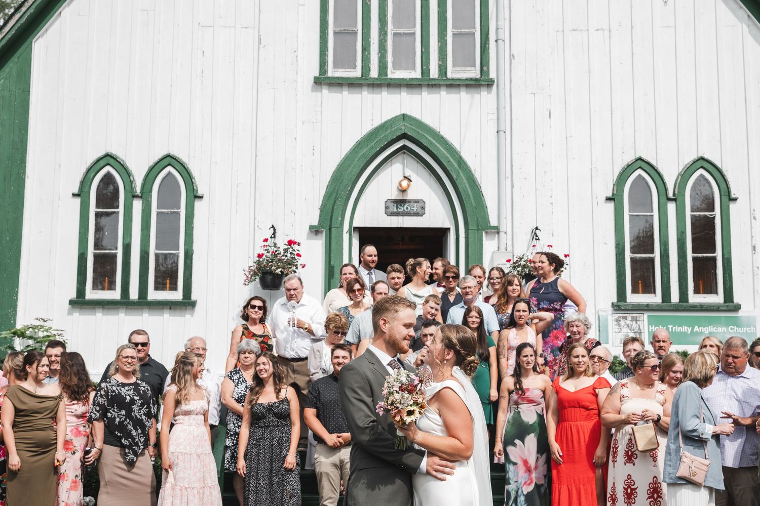 Invités du cortège de mariage posant ensemble devant un bâtiment blanc et vert pour une photo de groupe festive