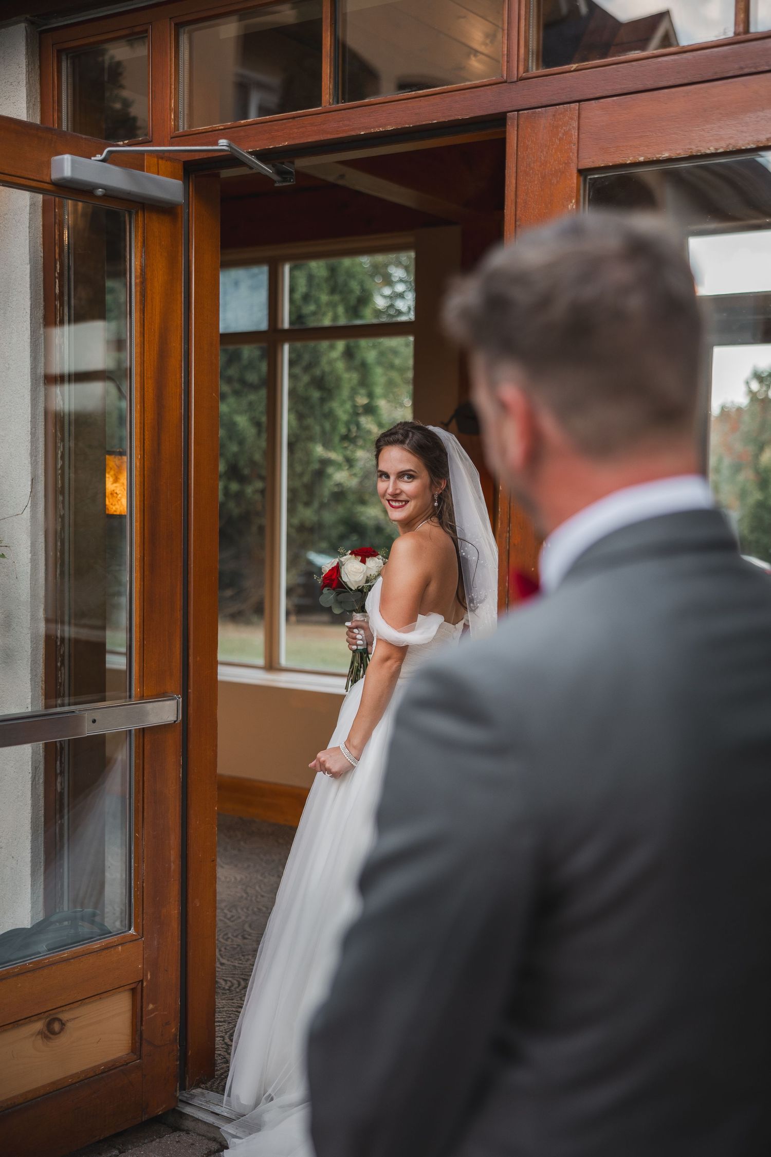 A bride in a white wedding dress looks back over her shoulder while standing in a wooden doorway entrance.