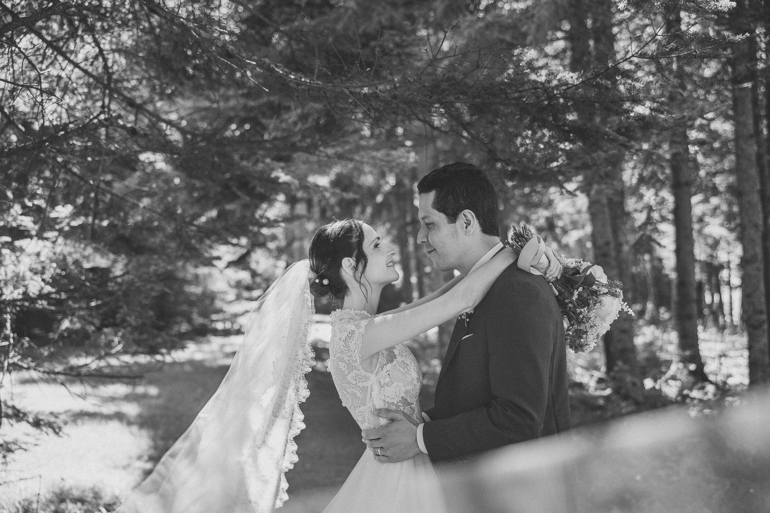 Photo de mariage montrant un noir et blanc s’enlaçant en extérieur, avec un bouquet floral blanc délicat.